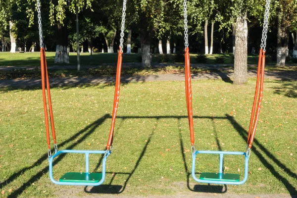 Bright gunga på en lekplats i parken. I djup skugga. En tom gunga. — Stockfoto