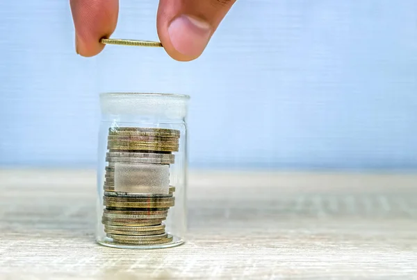 Mão de homem colocando uma moeda em uma pilha em um frasco de vidro . — Fotografia de Stock