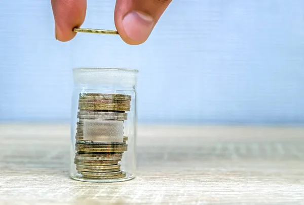 Mannens hand lägger ett mynt i en stapel i en glasburk. — Stockfoto