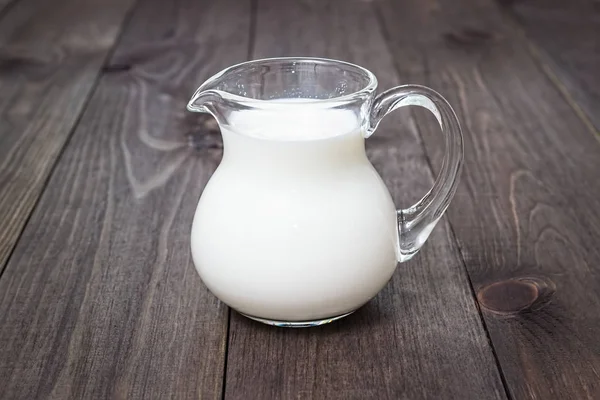 Milch in einem Glaskrug auf einem hölzernen Hintergrund. — Stockfoto