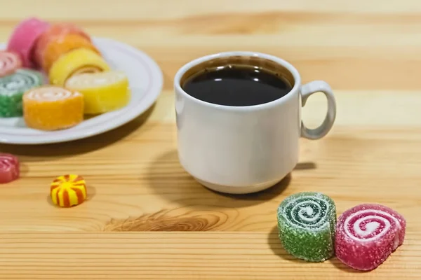 Fruit jelly and a cup of coffee on a gray wooden table.