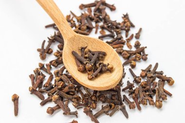 Baharat karanfil. Karanfil baharat. Bir tahta kaşık beyaz bir arka plan üzerinde izole karanfil yığını.