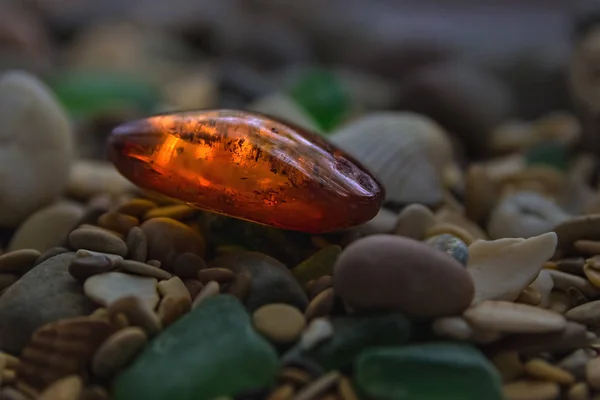 Bärnsten. Mineral gul. Kolofonium gul bärnsten. Sunstone på en strand med småsten. — Stockfoto