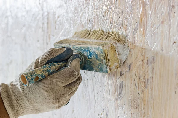 A man paints a wall. Painting  white paint. The hand in the glove uses a brush with paint.