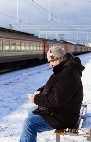 Ένας ηλικιωμένος άνδρας με ένα τηλέφωνο στο χέρι σε αναμονή για το τρένο — Φωτογραφία Αρχείου