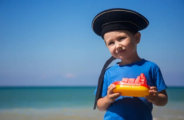 Criança adorável com barco de brinquedo contra o mar no dia ensolarado — Fotografia de Stock