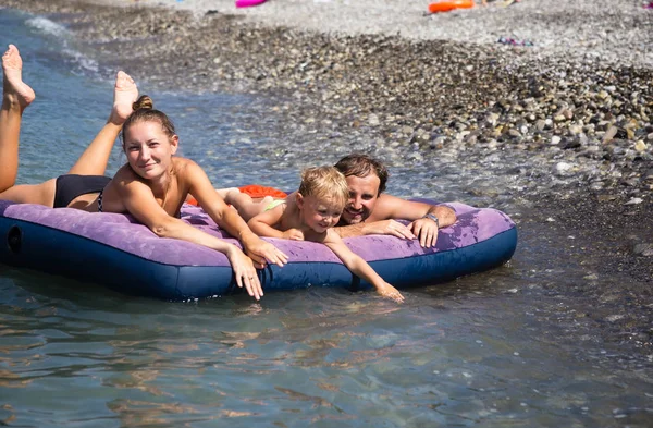 Família com filho flutuando em um colchão de ar no mar — Fotografia de Stock