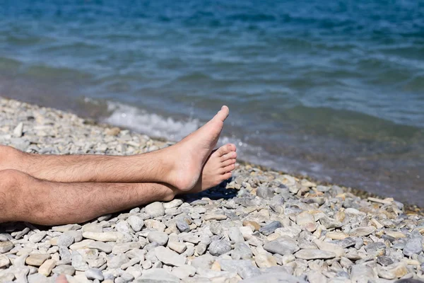 Erkekler ayakları üzerinde bir çakıl plajı deniz kenarında — Stok fotoğraf