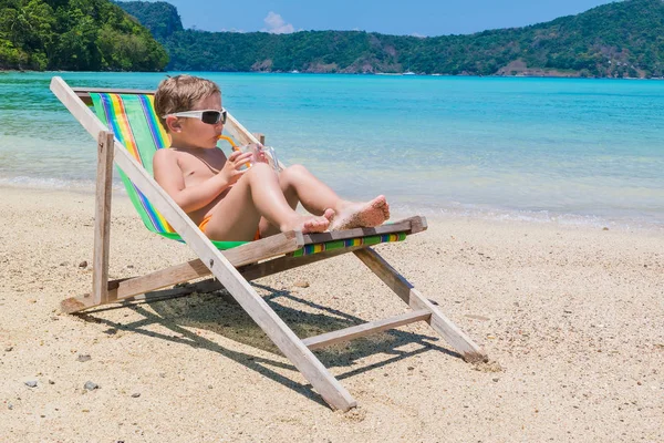 Ein kleiner Junge in Chaiselongue gegen das Meer, das Saft trinkt — Stockfoto