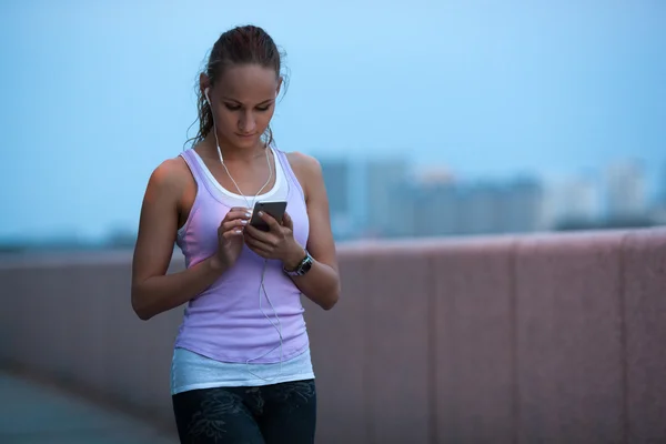 Ung atletisk sportig kvinna använder sin smartphone på kvällen — Stockfoto