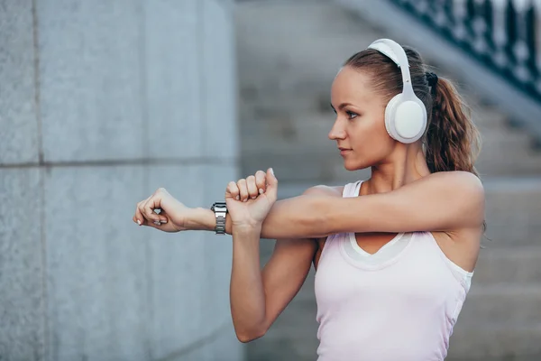 Młoda kobieta z słuchawki, przygotowanie do joggingu, ona jest rozciąganie jej ramienia. — Zdjęcie stockowe