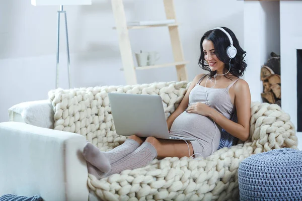Piękna młoda ciężarna kobieta z laptopem siedząca na kanapie w domu — Zdjęcie stockowe