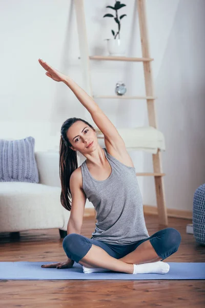 Junge fröhliche attraktive Frau, die Yoga praktiziert und in Sukhasana-Pose sitzt — Stockfoto