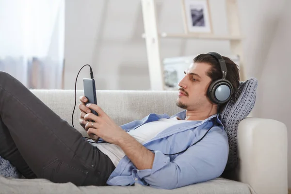 Bonito deitado no sofá com tablet e fones de ouvido — Fotografia de Stock