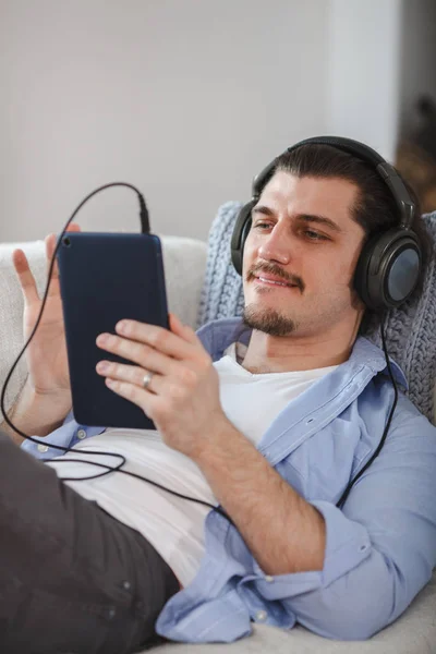 Bonito deitado no sofá com tablet e fones de ouvido — Fotografia de Stock