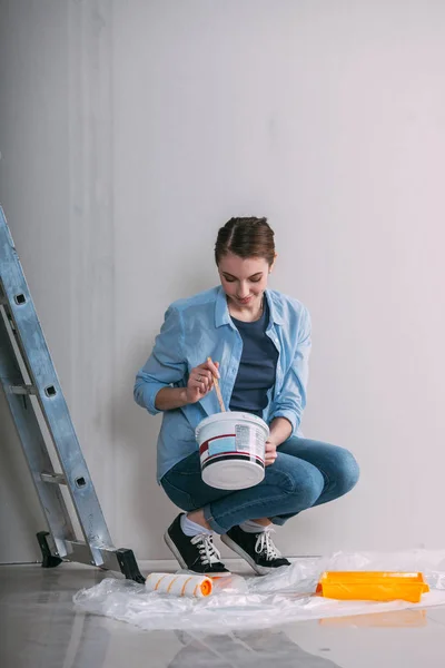 Woman sitting on the floor and mixing wall paint — Stock Photo, Image