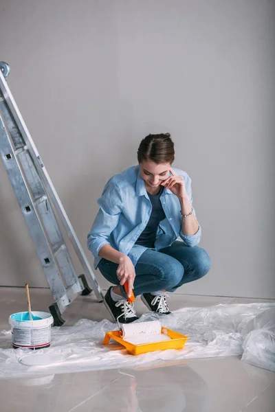 Woman sitting on the floor and draws paint on roller — Stock Photo, Image