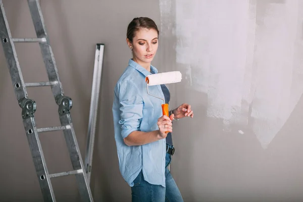 Beautiful young woman looking at wall and holding roller — Stock Photo, Image