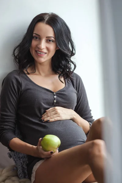 Aranyos boldog terhes nő ablakpárkányon almával a szobában, közelről — Stock Fotó