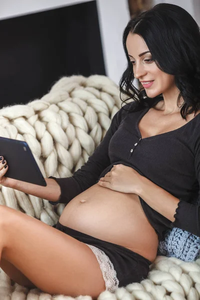 Щаслива вагітна жінка на дивані вдома, використовуючи цифровий планшет — стокове фото