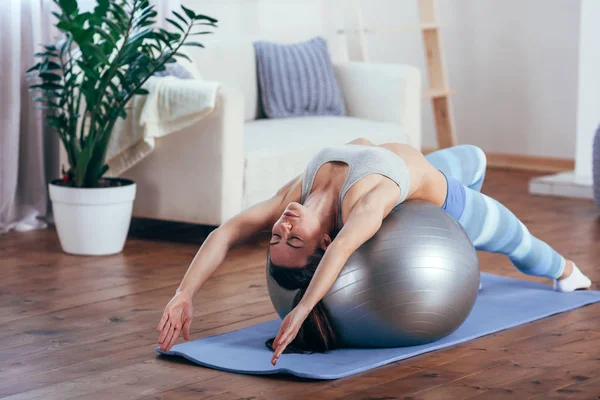 Young sportswoman doing exercises with ball on a mat at home — Stock Photo, Image