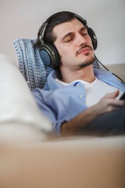 Yakışıklı adam kanepede tablet ve kulaklık ile yalan