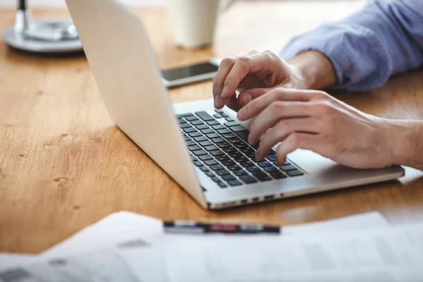Podnikatel, pracující v domácí kanceláři. Muž sedí dřevěná tabulka a pomocí moderní notebook, SMS zprávy klávesnice. — Stock fotografie