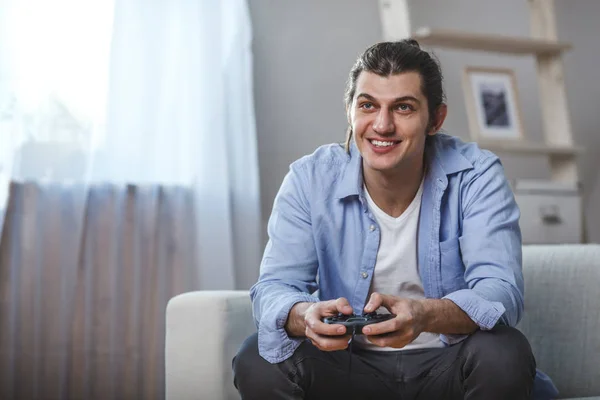 Joven sentado en un sofá jugando videojuegos dentro de su habitación —  Fotos de Stock