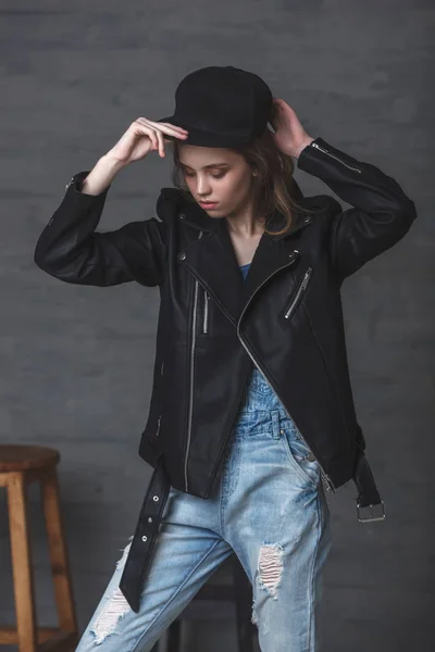 レザー ジャケット ジーンズと、暗い背景上のスタジオ ポートレートのキャップを身に着けている 10 代少女 — ストック写真