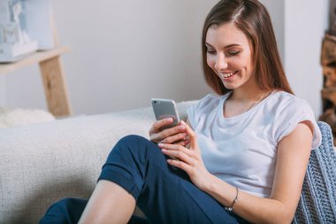 Genç kadın kanepede oturan akıllı telefonu kontrol