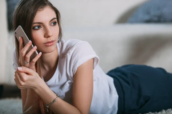 Молода жінка дзвонить через смартфон, лежачи на підлозі — стокове фото