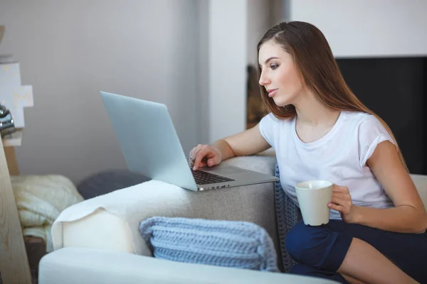 Jovem mulher sentada com laptop no sofá em sua casa — Fotografia de Stock