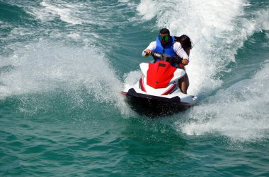 Maskeli adam kırmızı ve beyaz jet ski ile dalgalara biniyor..