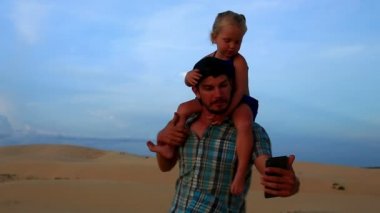 Closeup baba taşıyan küçük kız Selfie Dunes gökyüzü karşı yapar.