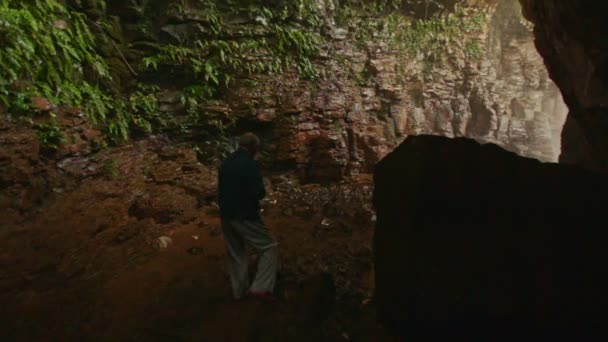 Старик с камерой проходит через темную скалистую пещеру — стоковое видео