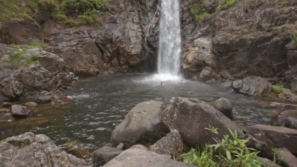 Мужчины плавают в реке возле водопада — стоковое видео