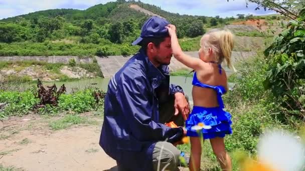 Padre se pone en cuclillas con hija con se quita la gorra — Vídeos de Stock