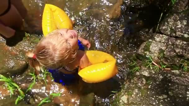特写镜头小金发碧眼的小金发女孩与辫子在黄色的臂章沐浴在透明的山河 — 图库视频影像