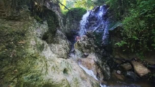 Baños de hombre bajo fuertes chorros de cascada entre rocas — Vídeo de stock