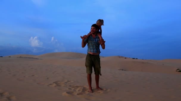 Отец гуляет с девушкой на плечах против дюн — стоковое видео