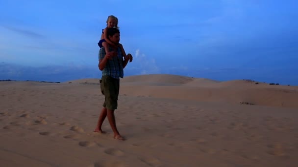 Отец гуляет с девушкой на плечах против дюн — стоковое видео