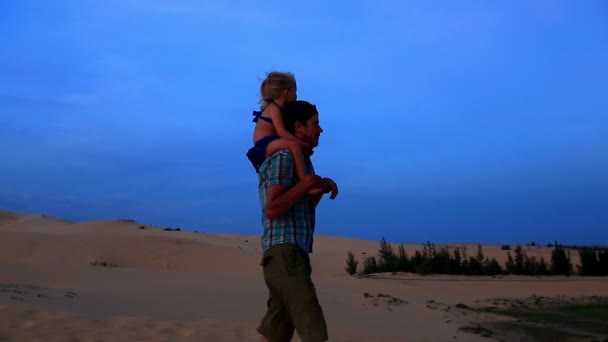 Отец гуляет с девочкой на плечах по дюнам — стоковое видео