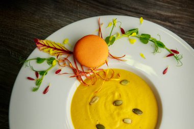 Derin beyaz plaka üzerinde turuncu macaron dekorasyon taze kabak krem çorbası