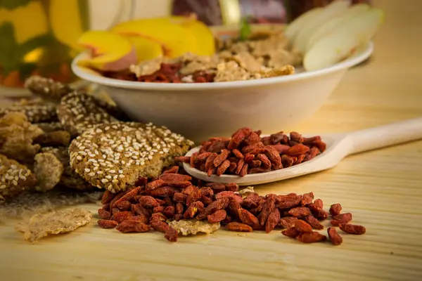 Bayas rojas de goji en una cuchara grande de madera cerca de un tazón grande con gachas — Foto de Stock