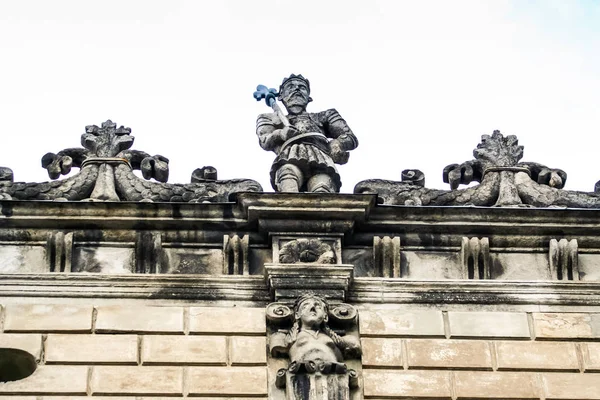 closeup man and animal stone sculptures on front facade of roof of age-old building