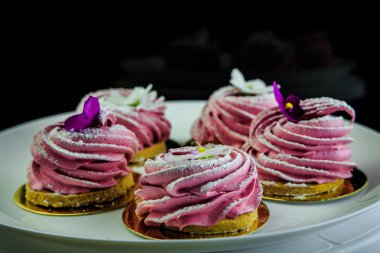 siyah arka plan beyaz tabakta mor çiçeklerle süslenmiş pembe zephyr kurabiye