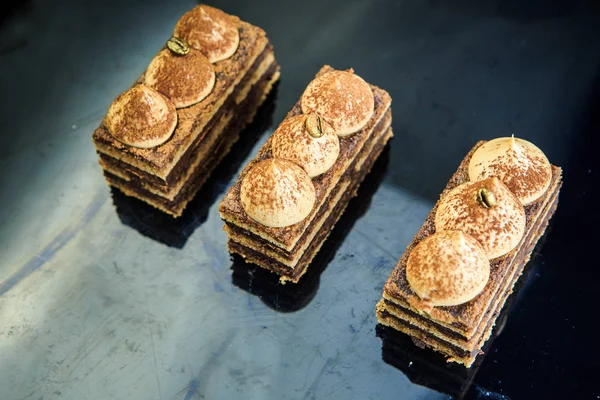 three chocolate opera cake slices decorated with white cream on black mirror background from above