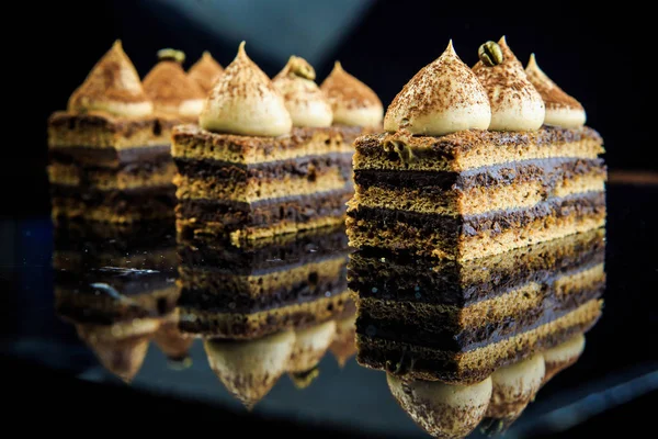 three chocolate opera cake slices decorated with white cream on black mirror background
