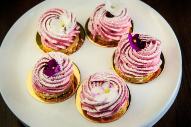 Yukarıdan beyaz tabakta mor çiçeklerle süslenmiş pembe zephyr kurabiye