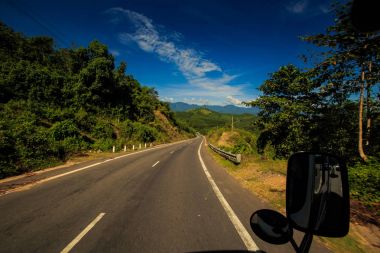 güneşli otoyol uzak tepeler ve mavi gökyüzü karşı yüksek tropik bitkiler arasında